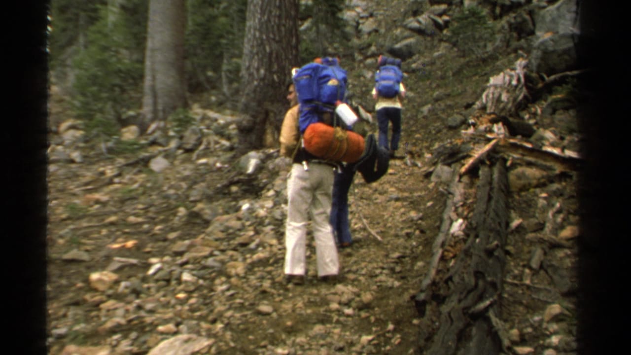 1978 Lake Tahoe frame with backpackers carrying large blue packs along a rocky pine forest trail.