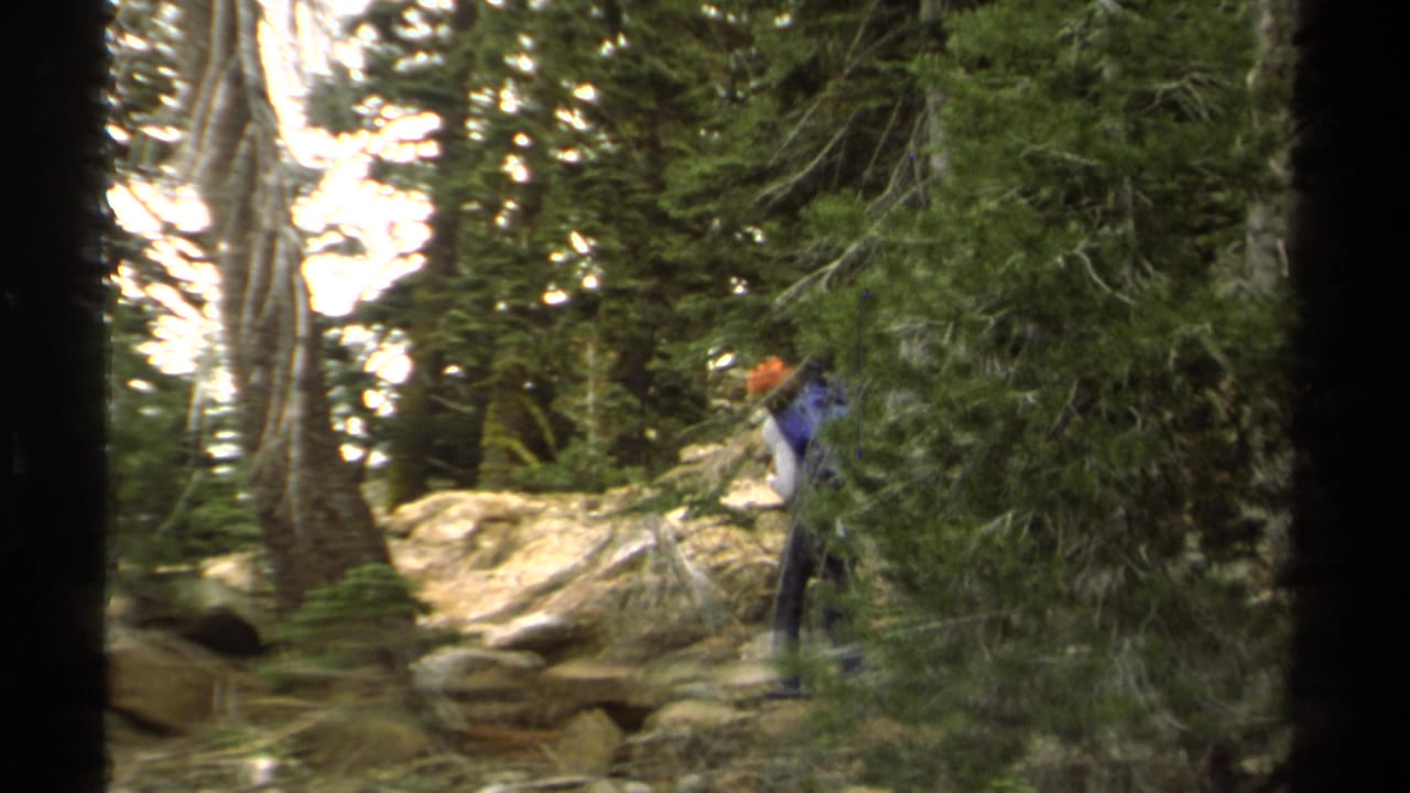 1978 Lake Tahoe frame of a hiker in an orange helmet and blue backpack ascending a rocky pine forest trail.