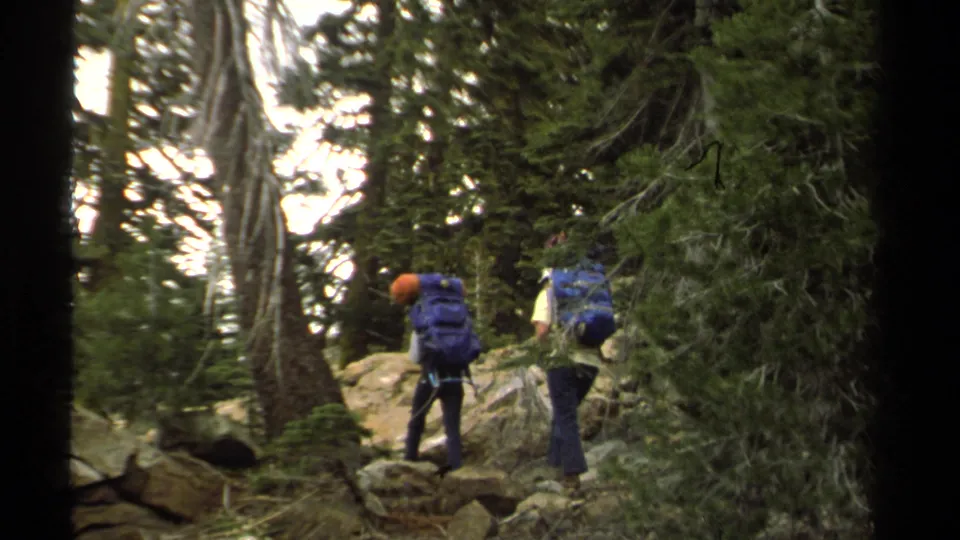 1978 Lake Tahoe frame showing two hikers with blue backpacks and orange helmets walking up a rocky forest trail.