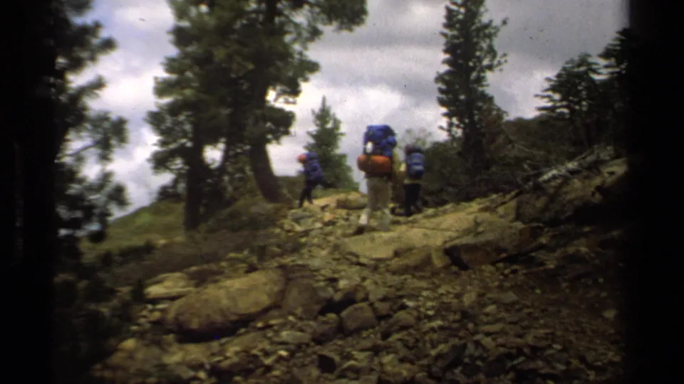 Several hikers with packs move along uneven rocks beneath tall trees in Lake Tahoe home-movie footage from 1978.