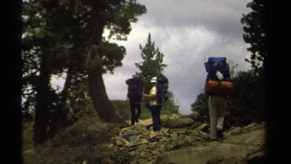 Three backpackers, seen from behind and side, navigate rocky terrain in 1978 Lake Tahoe home-movie footage.