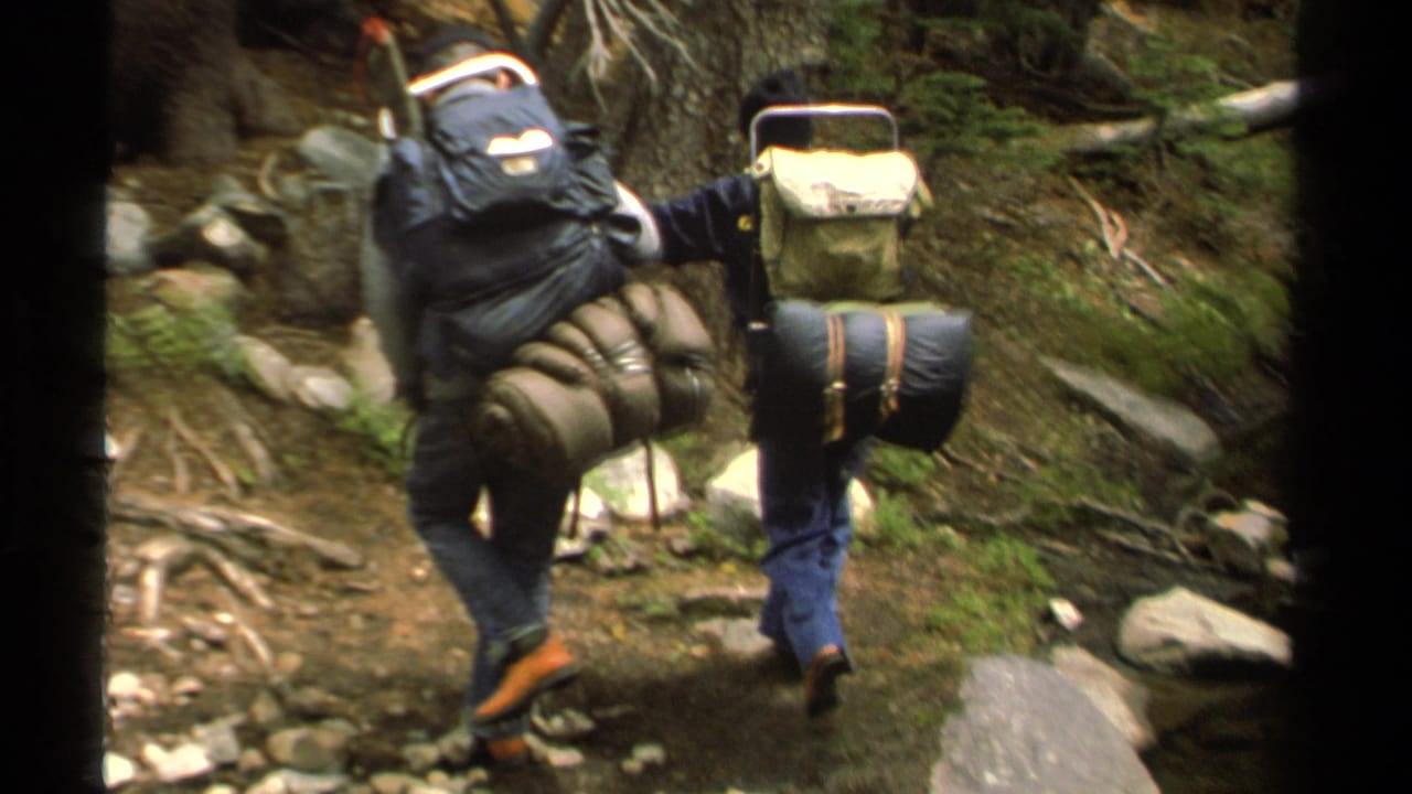 Lake Tahoe 1978 8mm frame of backpackers moving uphill on a rocky wooded trail near shallow water.