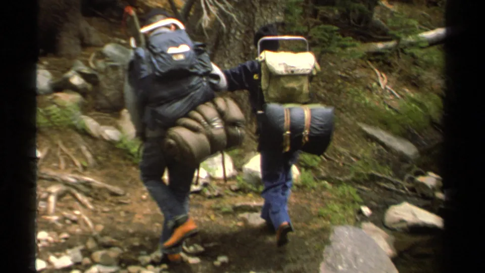 Lake Tahoe 1978 8mm frame of backpackers moving uphill on a rocky wooded trail near shallow water.