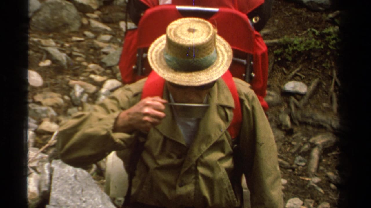 1978 Lake Tahoe home-movie frame showing a man in a straw hat and olive jacket on a rocky mountain trail with red hiking gear.