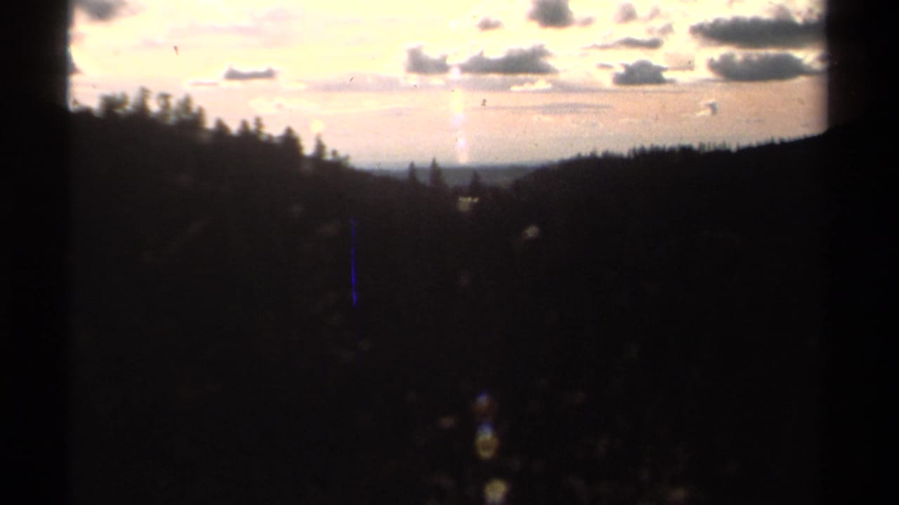 Dark forested valley beneath a bright sunset sky with clouds and film gate edges.