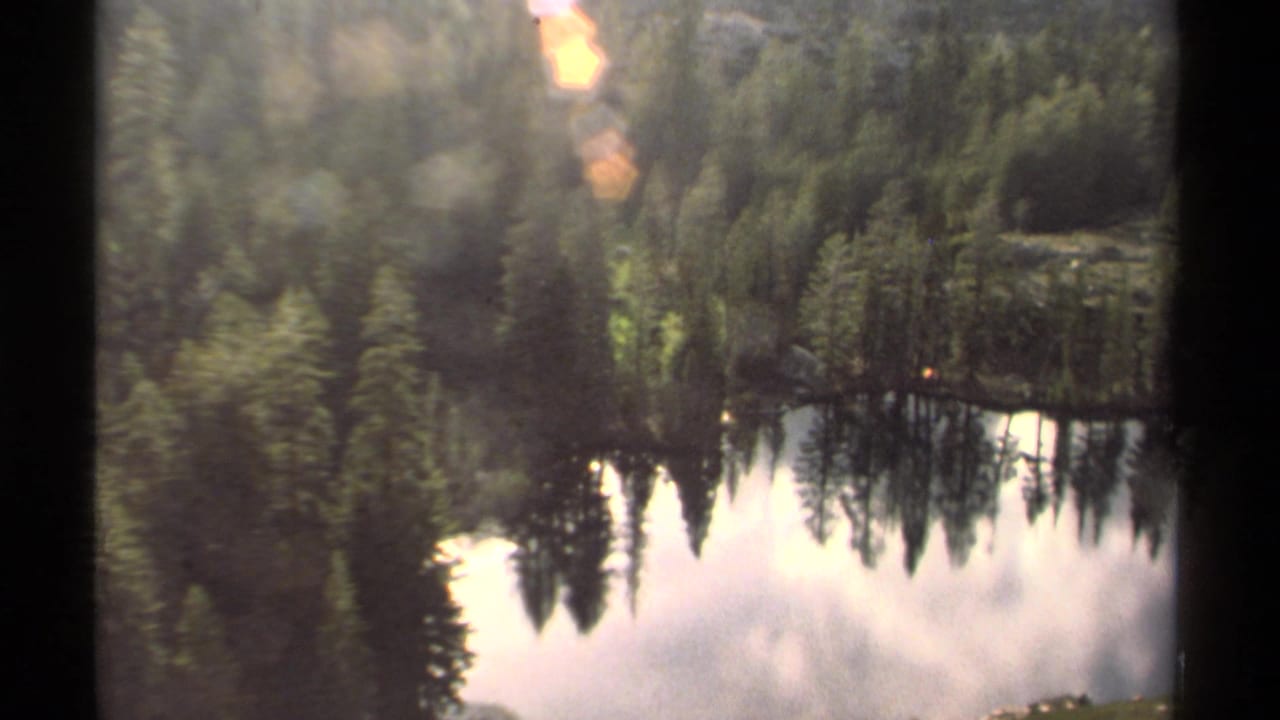 1978 Lake Tahoe 8mm frame showing evergreen trees, a small lakeside tent, and reflections across calm water.