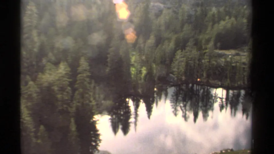1978 Lake Tahoe 8mm frame showing evergreen trees, a small lakeside tent, and reflections across calm water.
