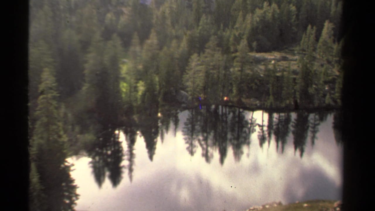 Lake Tahoe camping view on 8mm film with a tent among trees and a strong mirrored shoreline reflection.