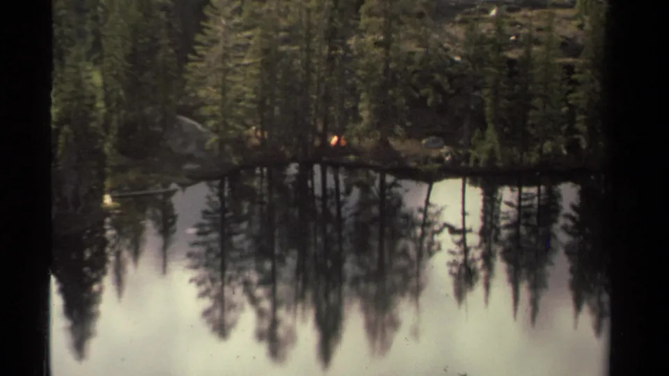 The zoom settles on the Lake Tahoe shore, where a small tent sits among evergreens above mirrored water.