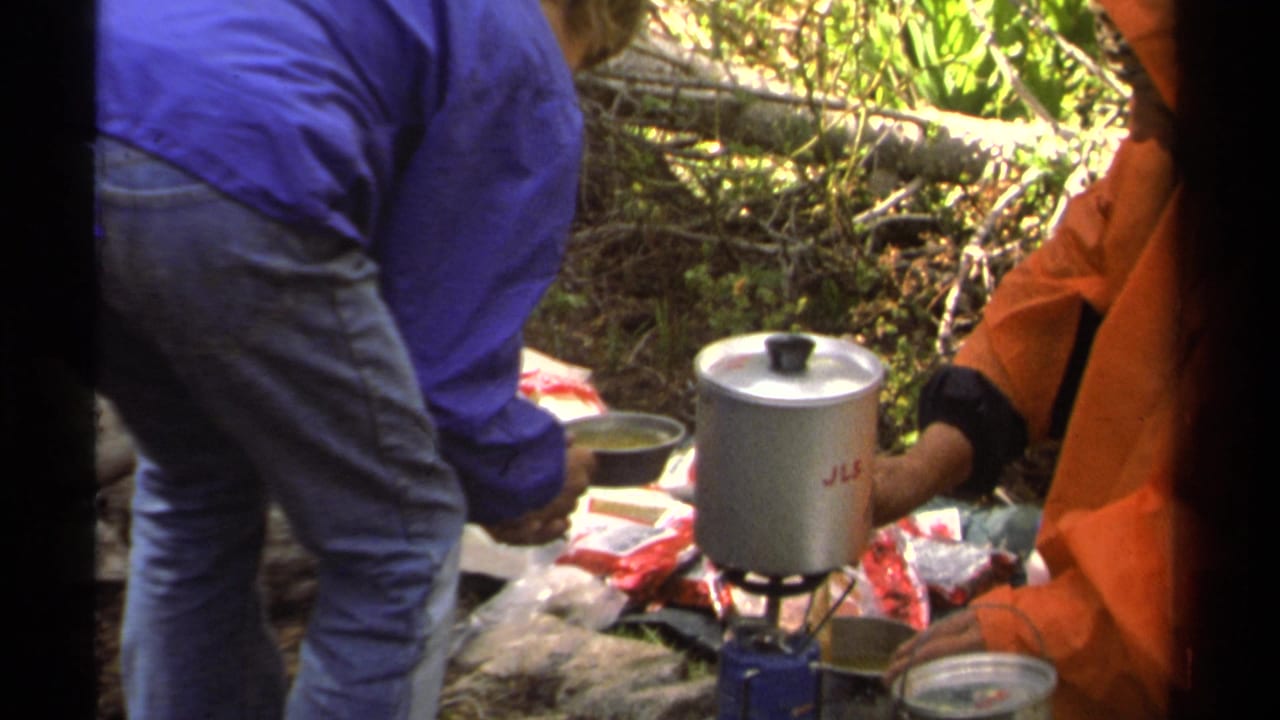 1978 Lake Tahoe camping footage shows people in blue and orange rain gear cooking beside a silver pot on a portable stove.