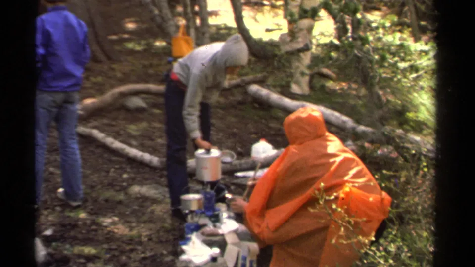1978 home-movie camping footage near Lake Tahoe shows people standing and crouching around cooking gear among logs and trees.