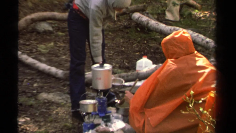 Lake Tahoe 1978 camping footage shows an orange-ponchoed camper beside pots, a blue stove, and a white jug on wooded ground.