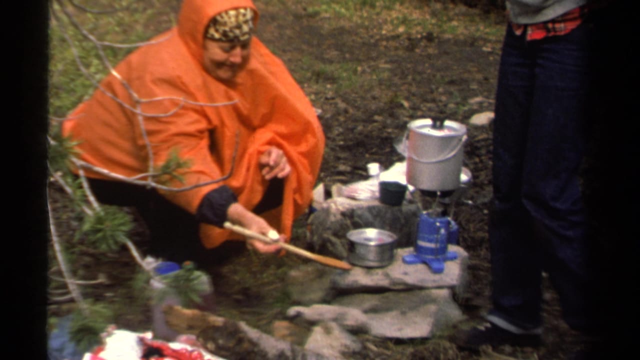 1978 Lake Tahoe camping footage showing a woman in an orange poncho tending food beside a blue gas stove and metal cookware.