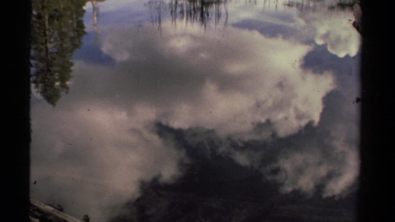 1978 Lake Tahoe 8mm frame showing inverted cloud and tree reflections on still water, with a fallen log along the lower edge.