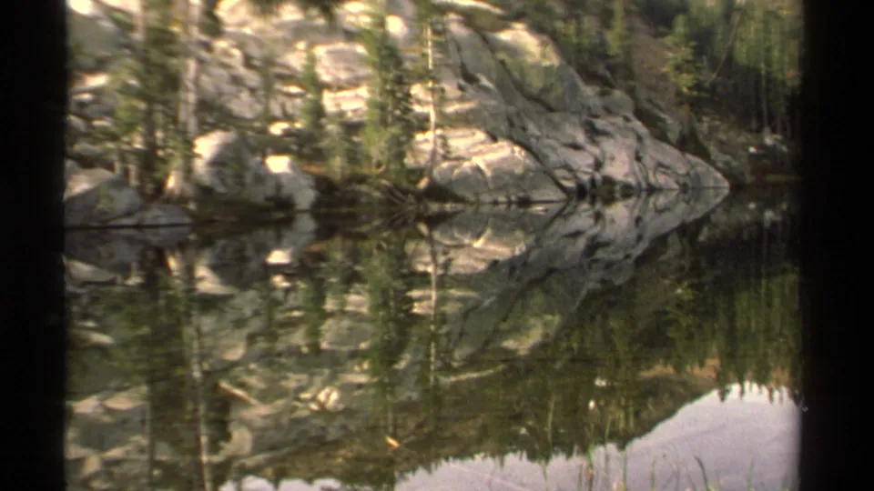 Lake Tahoe 8mm frame with still water, evergreen trees, and rocky shoreline mirrored across the surface.