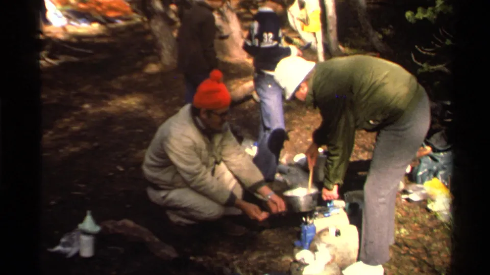 During a wooded Lake Tahoe stop, hikers handle cookware and a portable stove among scattered camping supplies.