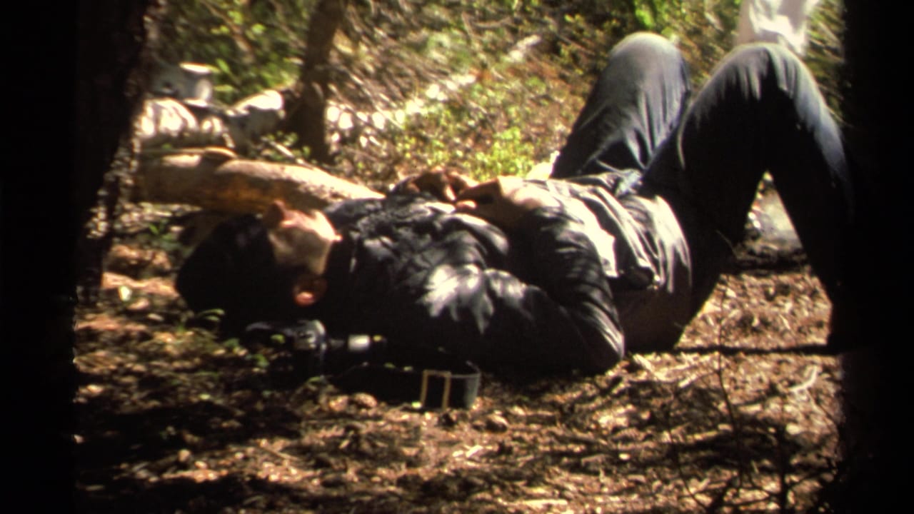 In 1978 Lake Tahoe home-movie footage, a man rests on the shaded forest floor in dappled sunlight.