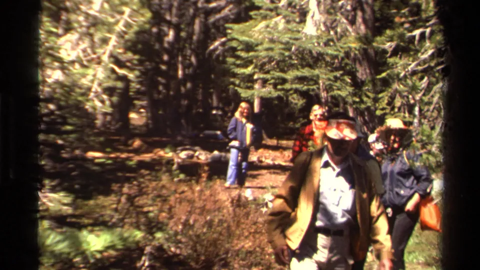 Lake Tahoe-area 1978 home-movie frame with a hat-wearing hiker close to camera and friends behind on a wooded path.