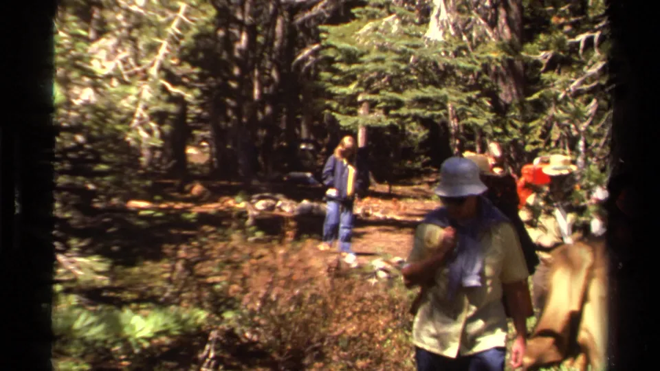 1978 8mm hiking scene near Lake Tahoe with adults in hats and backpacks moving past the camera in a pine forest.