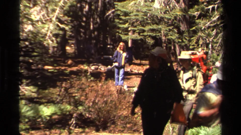 Lake Tahoe-area 1978 home movie frame showing hikers moving past the lens with a woman in a blue jacket in the forest background.