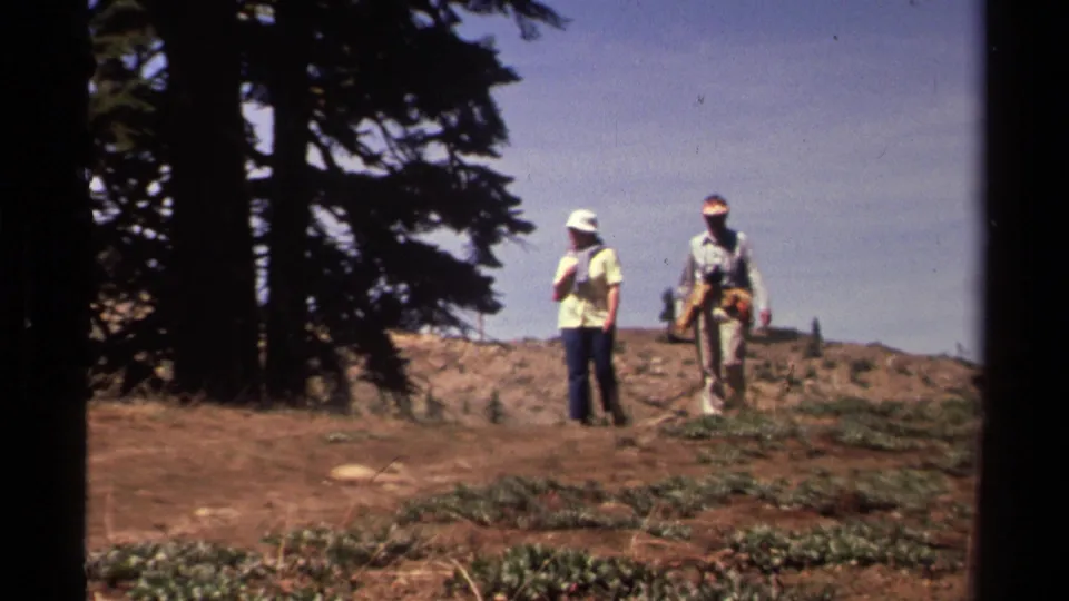 Two hikers in 1970s outdoor clothing walk along a dirt trail above a lake in the Lake Tahoe area.