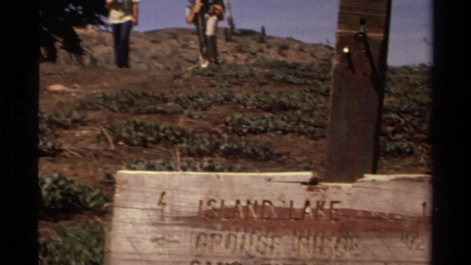 Wooden signpost on a Lake Tahoe area trail, with hikers nearby and text pointing toward Island Lake, Grouse Ridge, and Sand Ridge.