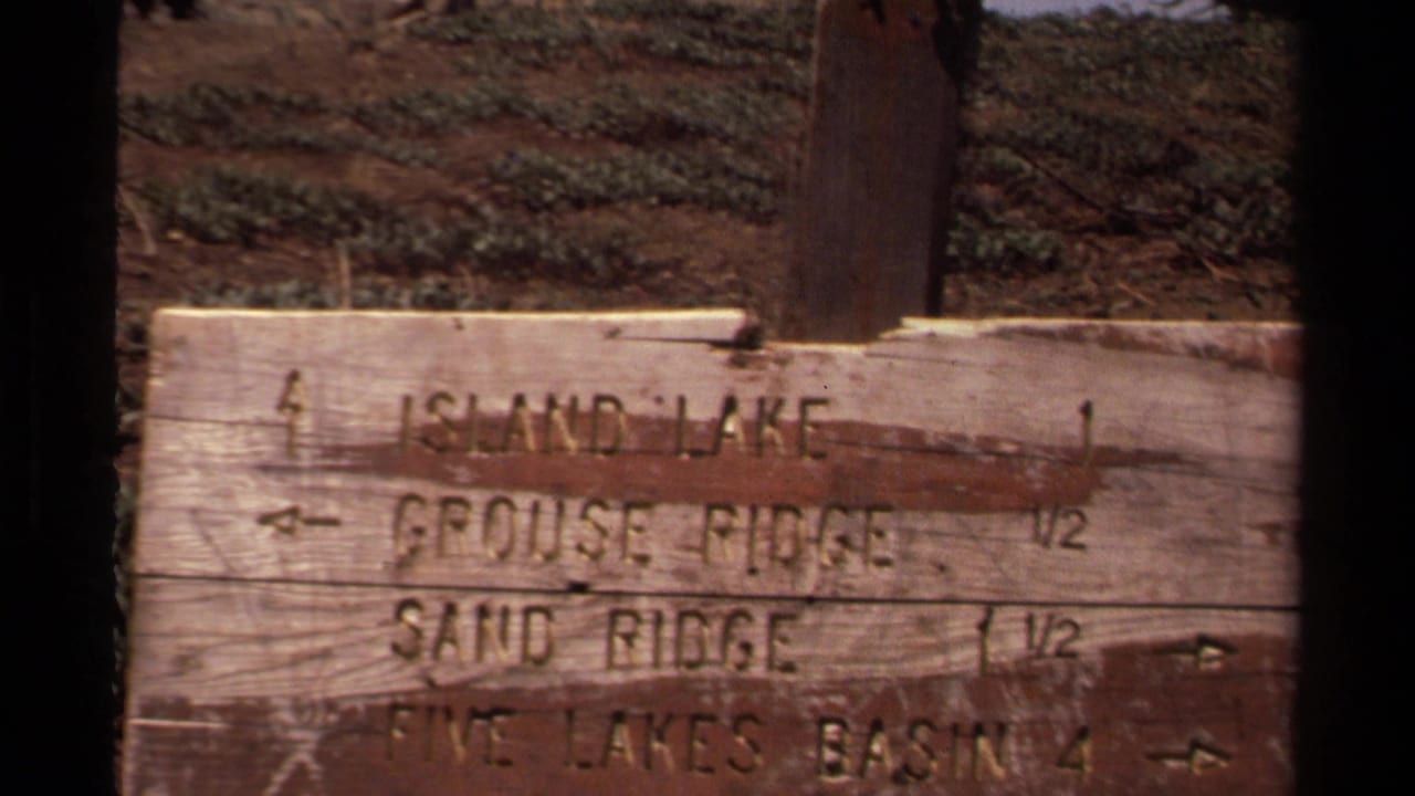 1978 Lake Tahoe-area 8mm frame showing a worn wooden trail sign with directional text for nearby ridges, lakes, and basin routes.