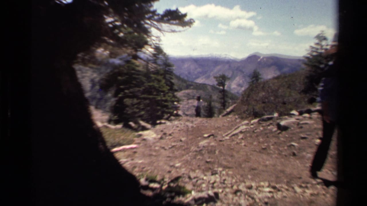 1978 Lake Tahoe home-movie frame showing a rocky trail, pine trees, distant mountain ridges, and a partially visible hiker.