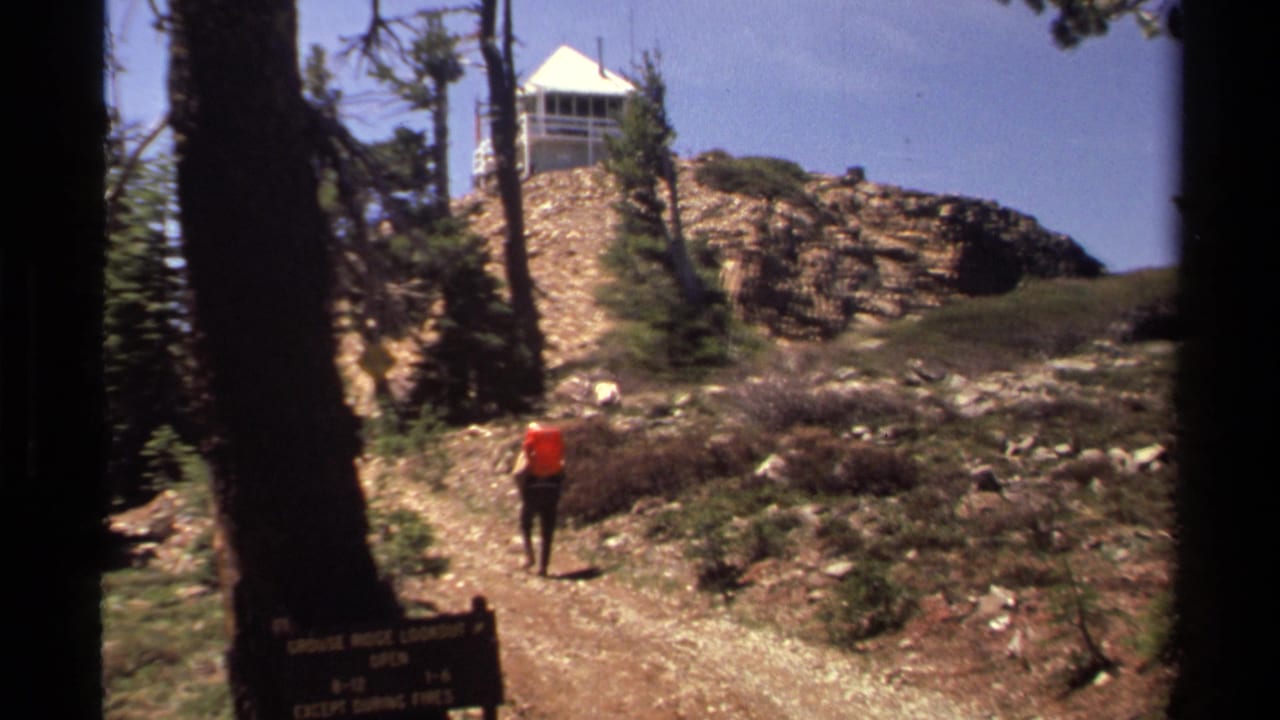 Hiker in orange walking up a rocky trail toward a white tower.