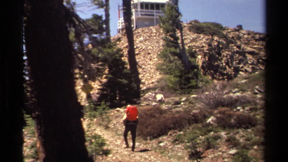 The orange-shirted hiker continues uphill below a white lookout tower in Lake Tahoe, California.