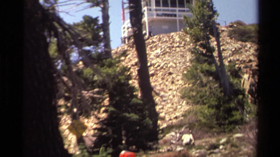 Pine trees frame the rocky slope and white lookout tower in 1978 Lake Tahoe home-movie footage.