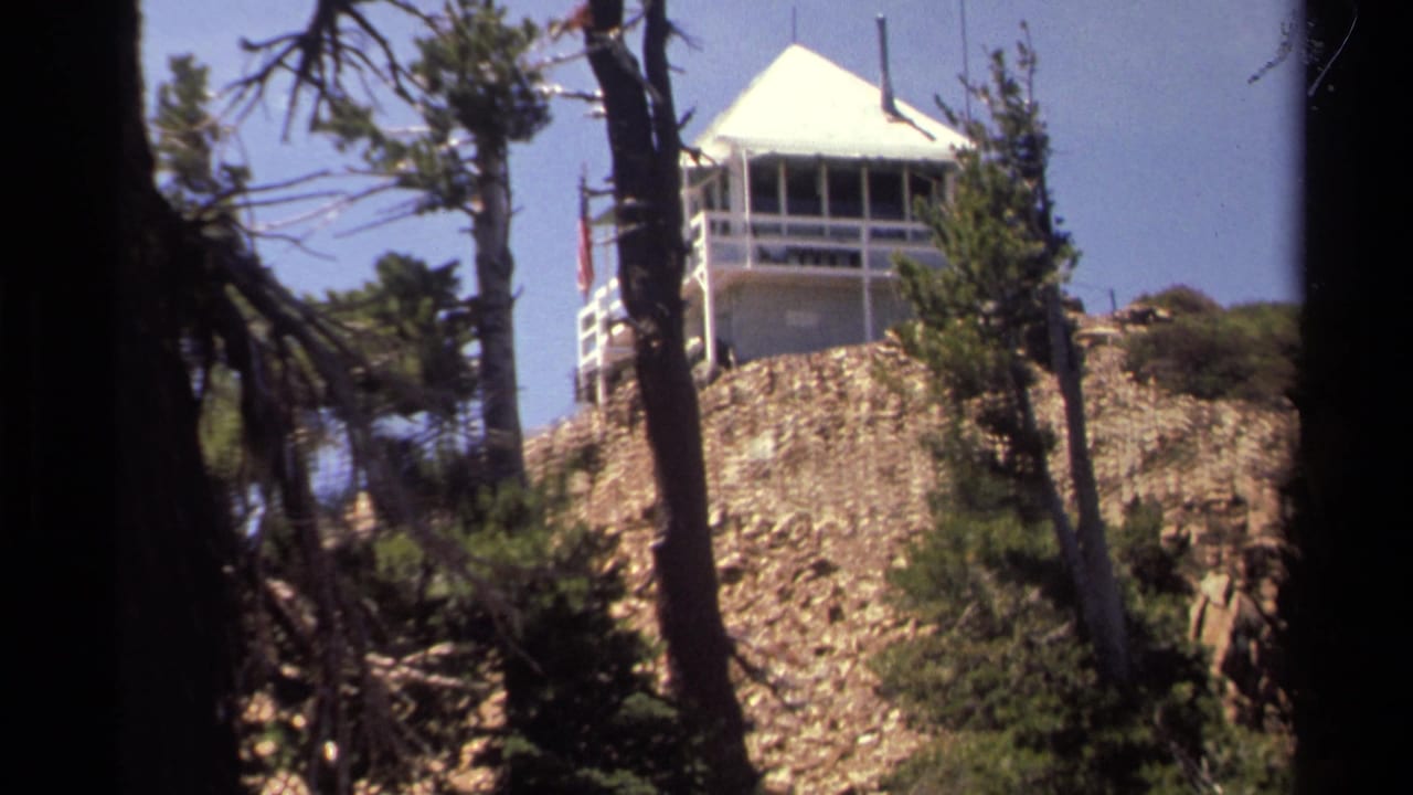 1978 Lake Tahoe home-movie frame showing a white lookout tower above a rocky hillside, partially obscured by pine trunks.