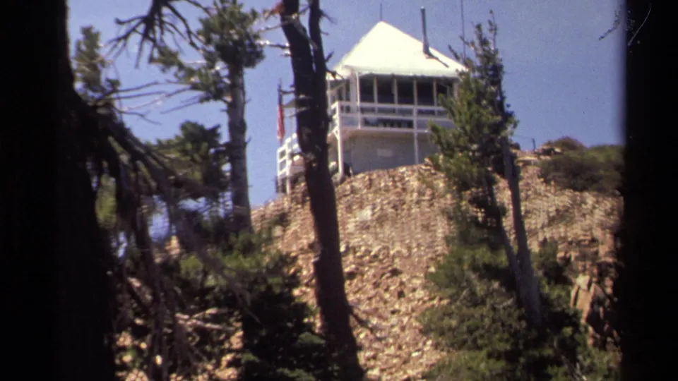 1978 Lake Tahoe home-movie frame showing a white lookout tower above a rocky hillside, partially obscured by pine trunks.