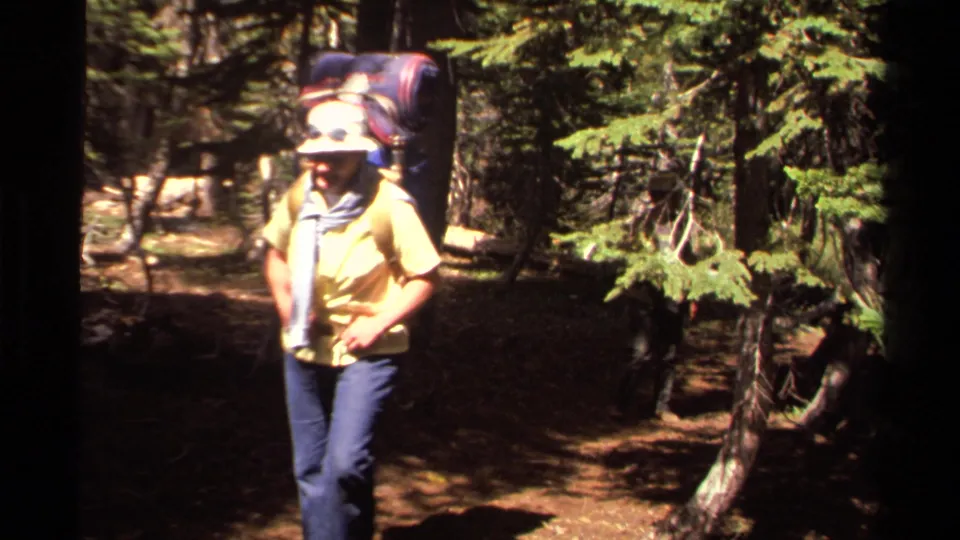 1978 Lake Tahoe home-movie frame showing a hiker in a yellow shirt carrying a large backpack through pine trees.