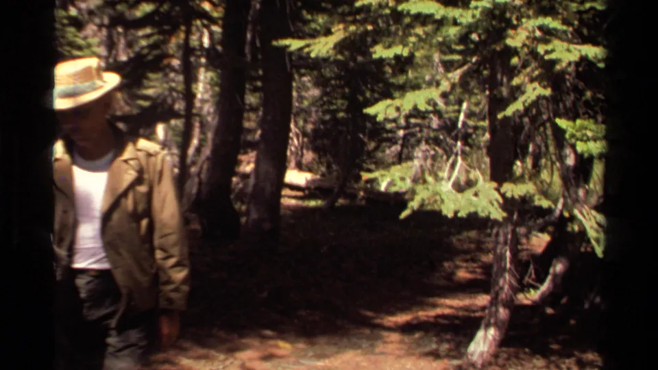 1978 Lake Tahoe home-movie frame showing a man in a straw hat partly framed at the edge of a pine forest scene.