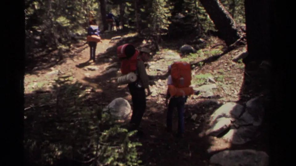 1978 Lake Tahoe 8mm frame showing two heavily loaded hikers from behind as another backpacker continues ahead on the path.