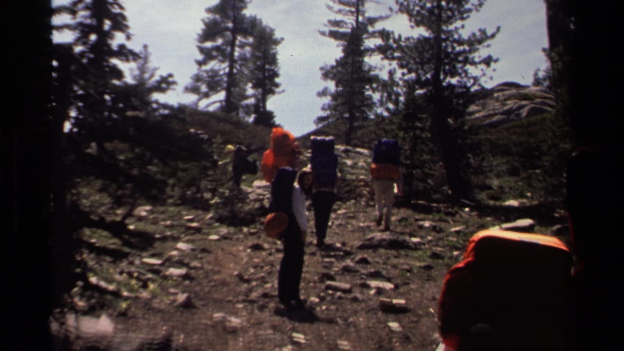 1978 Lake Tahoe frame of hikers with large packs crossing a rocky wooded trail in strong sunlight and shadow.