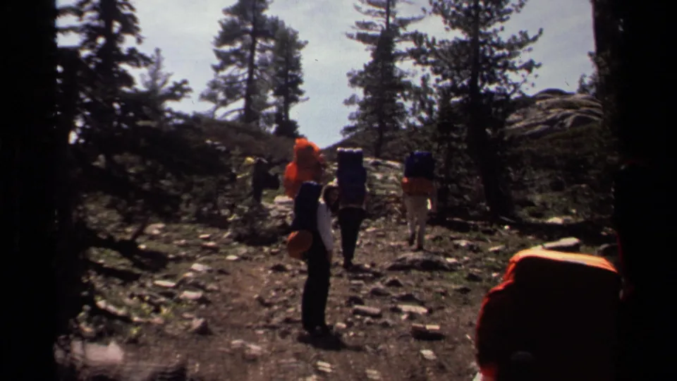 1978 Lake Tahoe frame of hikers with large packs crossing a rocky wooded trail in strong sunlight and shadow.