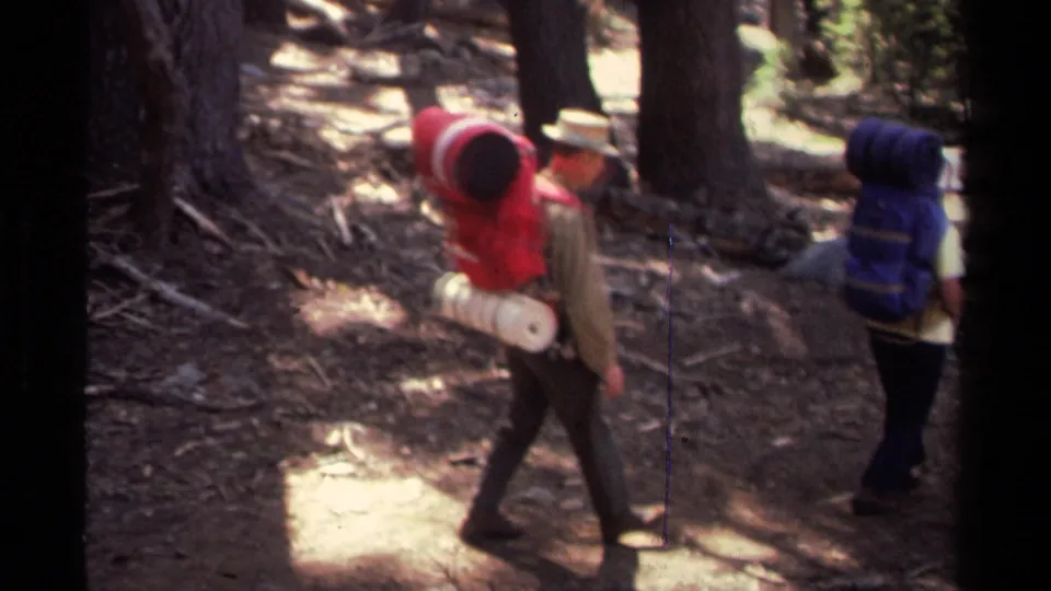 1978 Lake Tahoe frame showing hikers with rolled sleeping gear and large backpacks passing beneath tall trees.