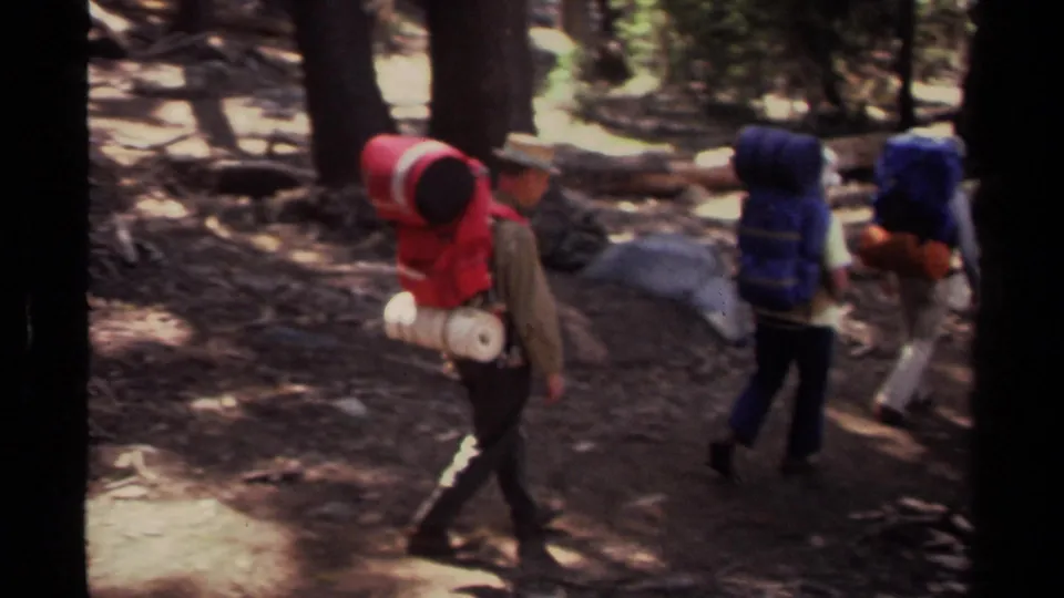 In 1978 Lake Tahoe footage, several hikers with large packs move along a sun-dappled forest path.