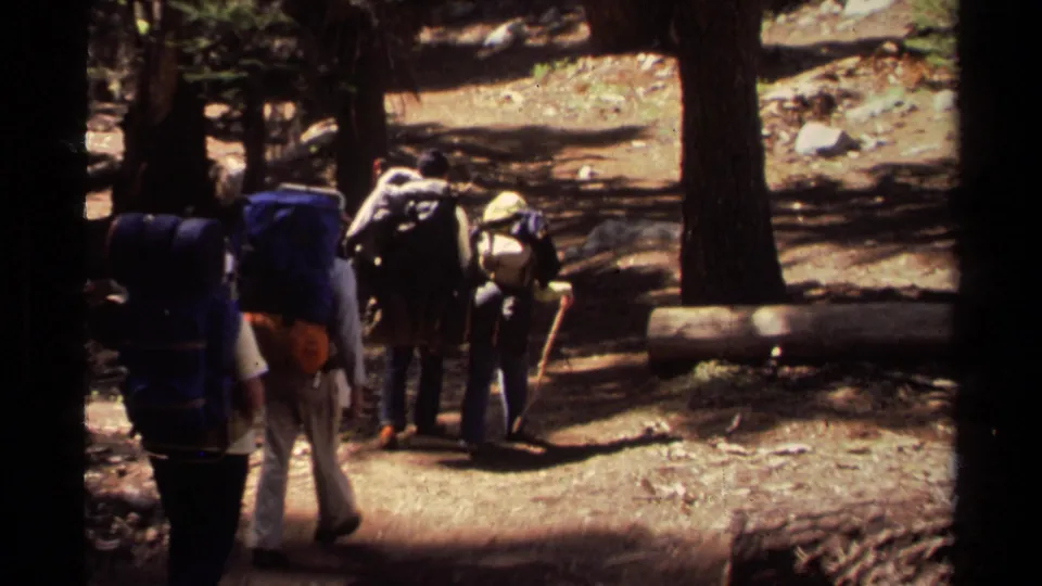 Backpackers seen from behind follow a shaded dirt path through Lake Tahoe forest in 1978 home-movie footage.