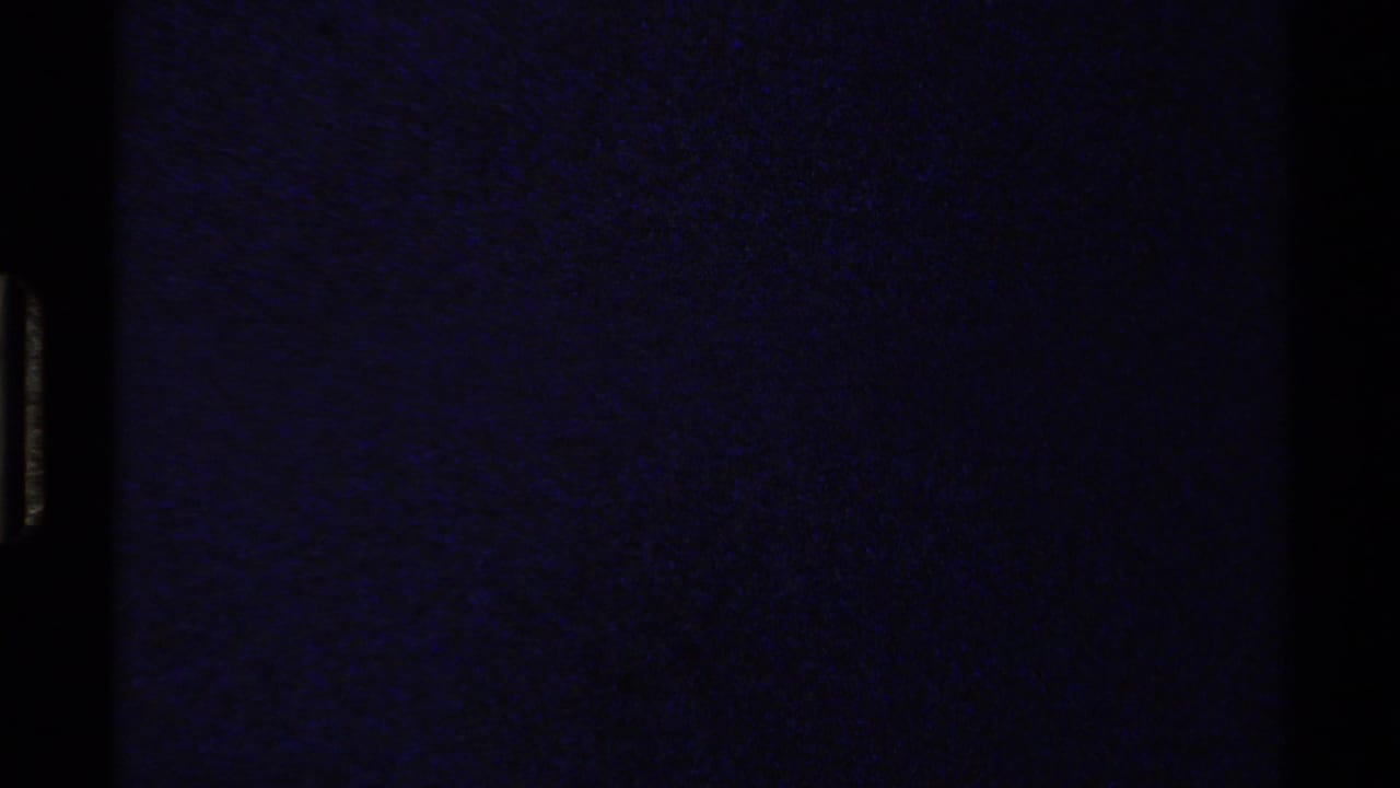 Mostly dark film frame with a narrow strip of outdoor scene at the right edge.