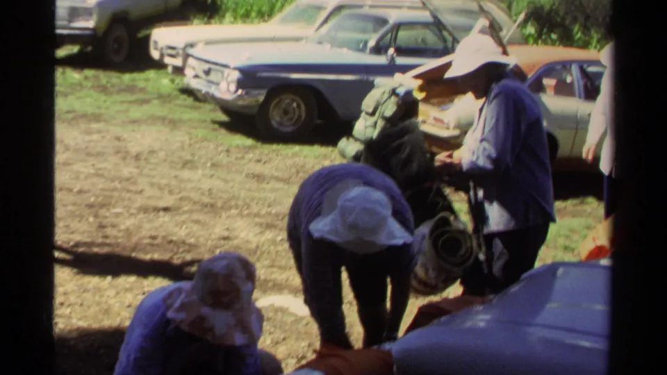 Lake Tahoe 1978 home-movie frame showing hikers in hats handling backpacks and gear beside several parked cars.