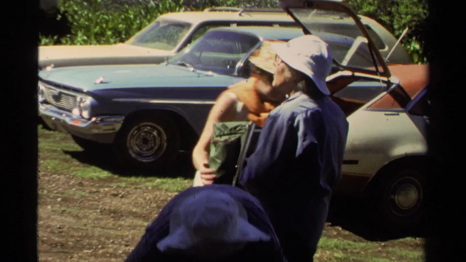 Two adults at Lake Tahoe in 1978 appear to prepare a pack near open car doors and older parked cars.