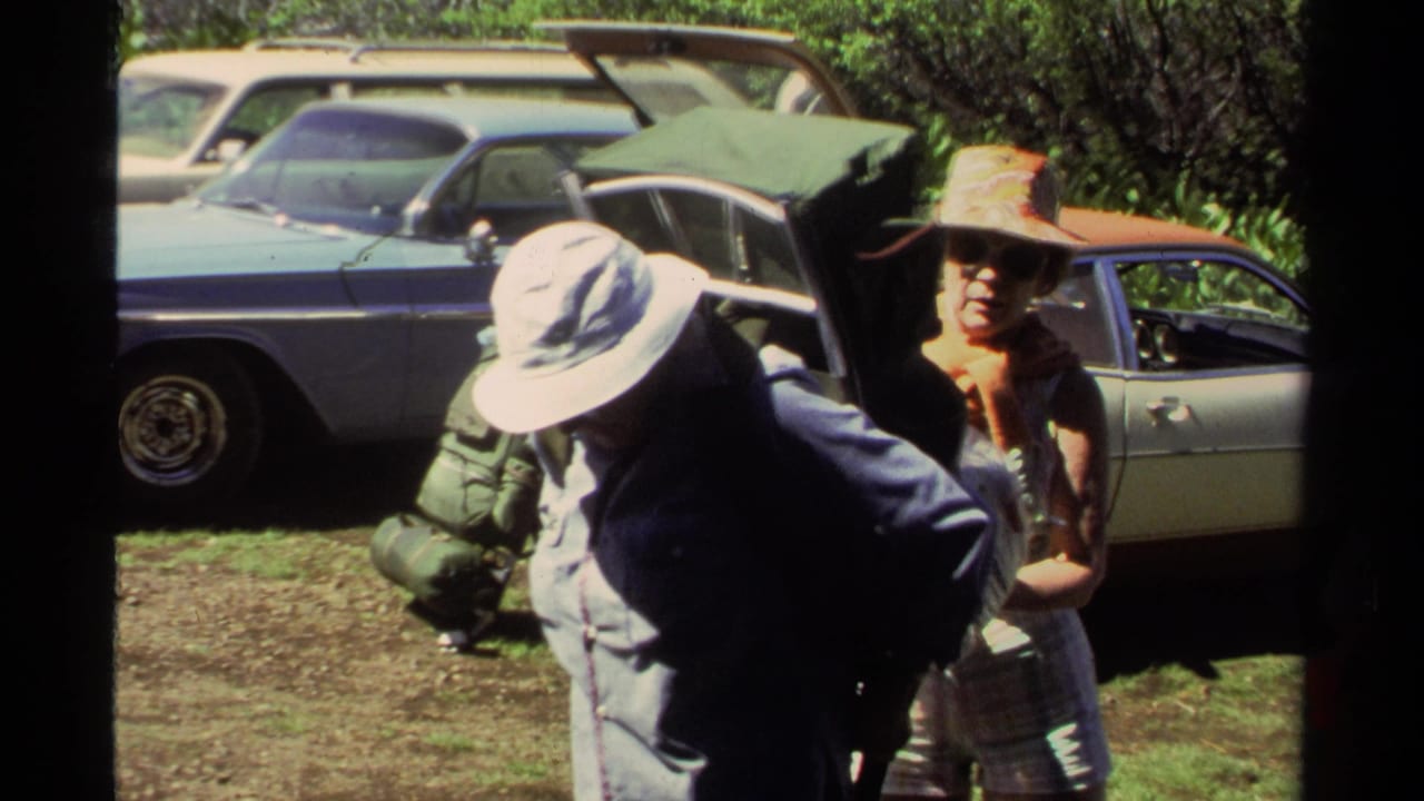 1978 Lake Tahoe frame of adults adjusting backpacks beside cars, with one person bent forward under a white sun hat.