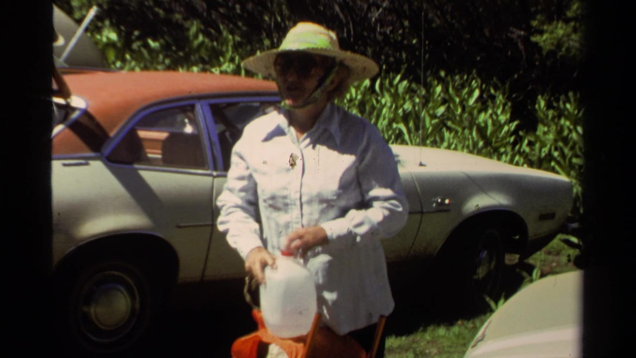 At Lake Tahoe in 1978, a woman in a wide-brim hat holds a water jug near a parked classic car in bright sun.