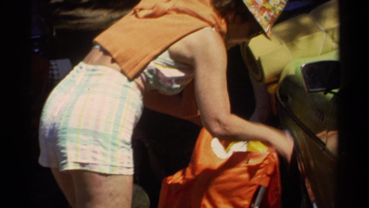 1978 Lake Tahoe-area home-movie frame of a woman in summer clothing packing an orange bag beside a green car.