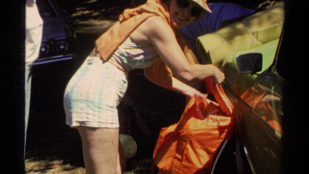 Woman in 1970s summer clothing handles an orange bag beside a vintage-looking green car in Lake Tahoe metadata context.