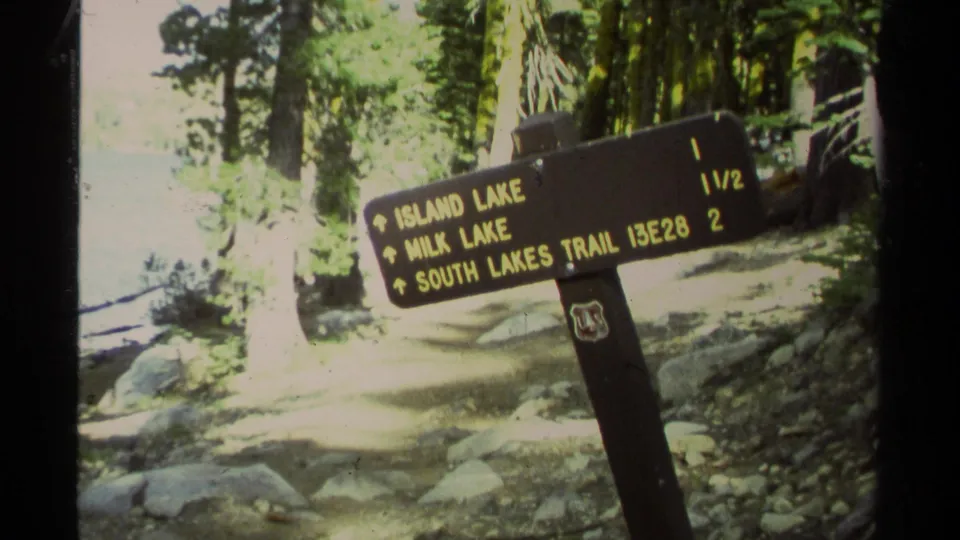 Close view of a forest trail sign with Island Lake, Milk Lake, and South Lakes Trail directions in the Lake Tahoe clip context.