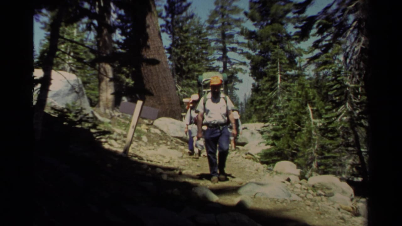 1978 Lake Tahoe 8mm frame of hikers with backpacks moving along a shaded rocky trail through pine forest.